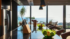 Une cuisine moderne dotée d’un grand îlot central, d’appareils électroménagers en acier inoxydable et offrant une vue sur la mer.