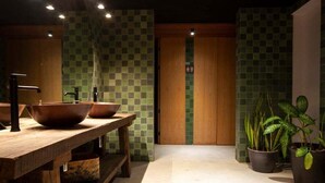 Des toilettes avec un banc en bois, un grand lavabo et des plantes en pot.