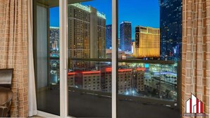 A room with a large window overlooking a cityscape at night, featuring illuminated buildings and a view of the street below. - MGM Signature- F1 Track Jacuzzi Strip View Balcony (Las Vegas)