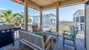 A covered outdoor deck with a grill, seating, and a view of the beach and buildings. - The almost seamless integration of outside and inside makes this the picture-per (Port Aransas)