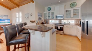 A modern kitchen with white cabinetry, a central island with bar stools, a large window, and a wooden ceiling. - The almost seamless integration of outside and inside makes this the picture-per (Port Aransas)