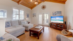 A spacious living room with a wooden ceiling, a large flat-screen TV, a wooden coffee table, and a comfortable seating area with a sofa and ottoman. - The almost seamless integration of outside and inside makes this the picture-per (Port Aransas)