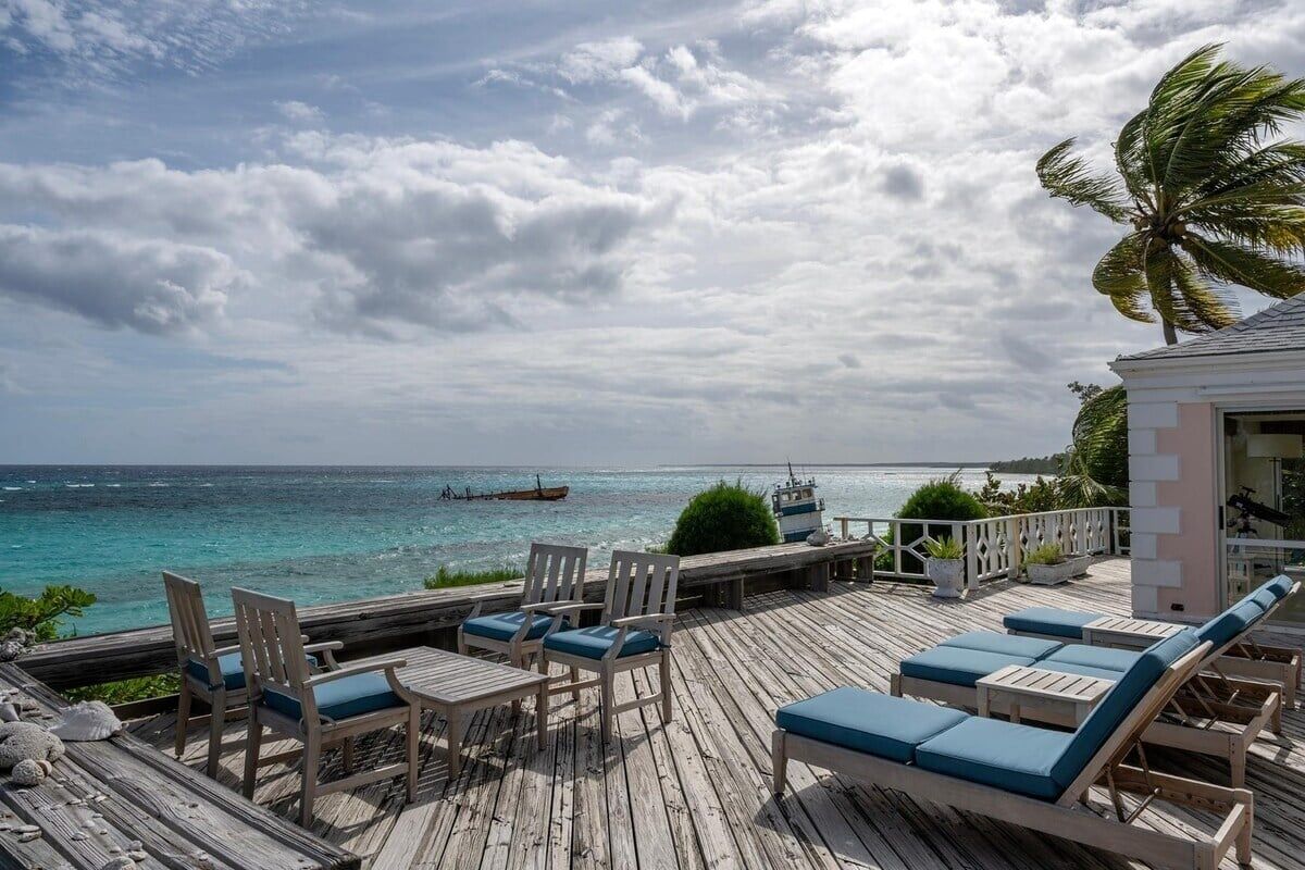 A wooden deck with lounge chairs and tables overlooking a turquoise sea.