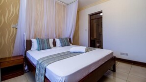 A bedroom with a large bed, white curtains, and a wooden headboard.