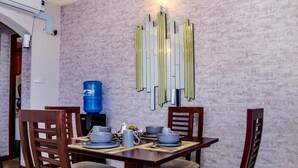 A dining area with a table set for four, chairs, a water dispenser, and a decorative wall piece.