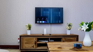 A modern living room with a flat-screen TV mounted on the wall, a wooden entertainment unit with a cabinet, and two potted plants.