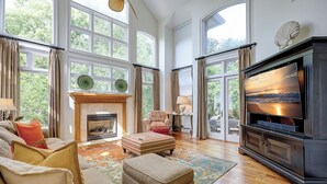 A spacious living room with a fireplace, large windows, and a television. - 12 Port Tack -  4 min walk to the ocean.  Views of golf, lagoons & sunset (Hilton Head Island)