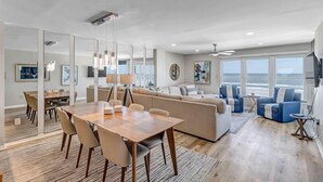 Un vaste espace de vie comprenant une table à manger en bois, des canapés beige et des fauteuils bleus.