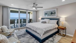 Une chambre dotée d’un grand lit, d’un ventilateur de plafond, d’une vue sur l’extérieur et d’un balcon avec des chaises.