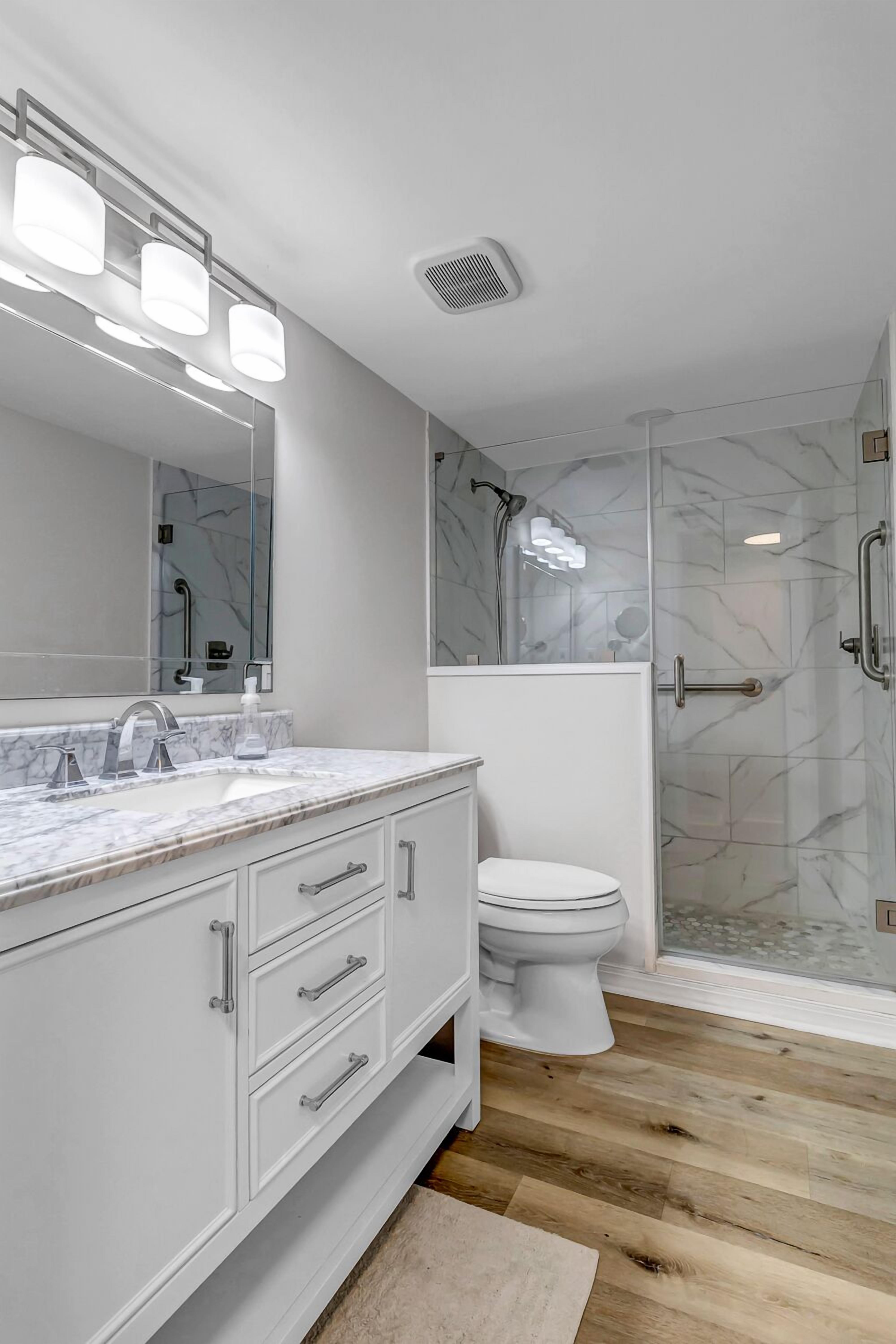 A modern bathroom with a marble vanity, a toilet, and a glass-enclosed shower.