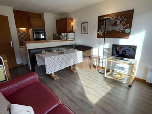 Un espacio habitable compacto con comedor, un sofá rojo, un televisor sobre un mueble bajo y una zona de cocina con armarios de madera y un microondas.
