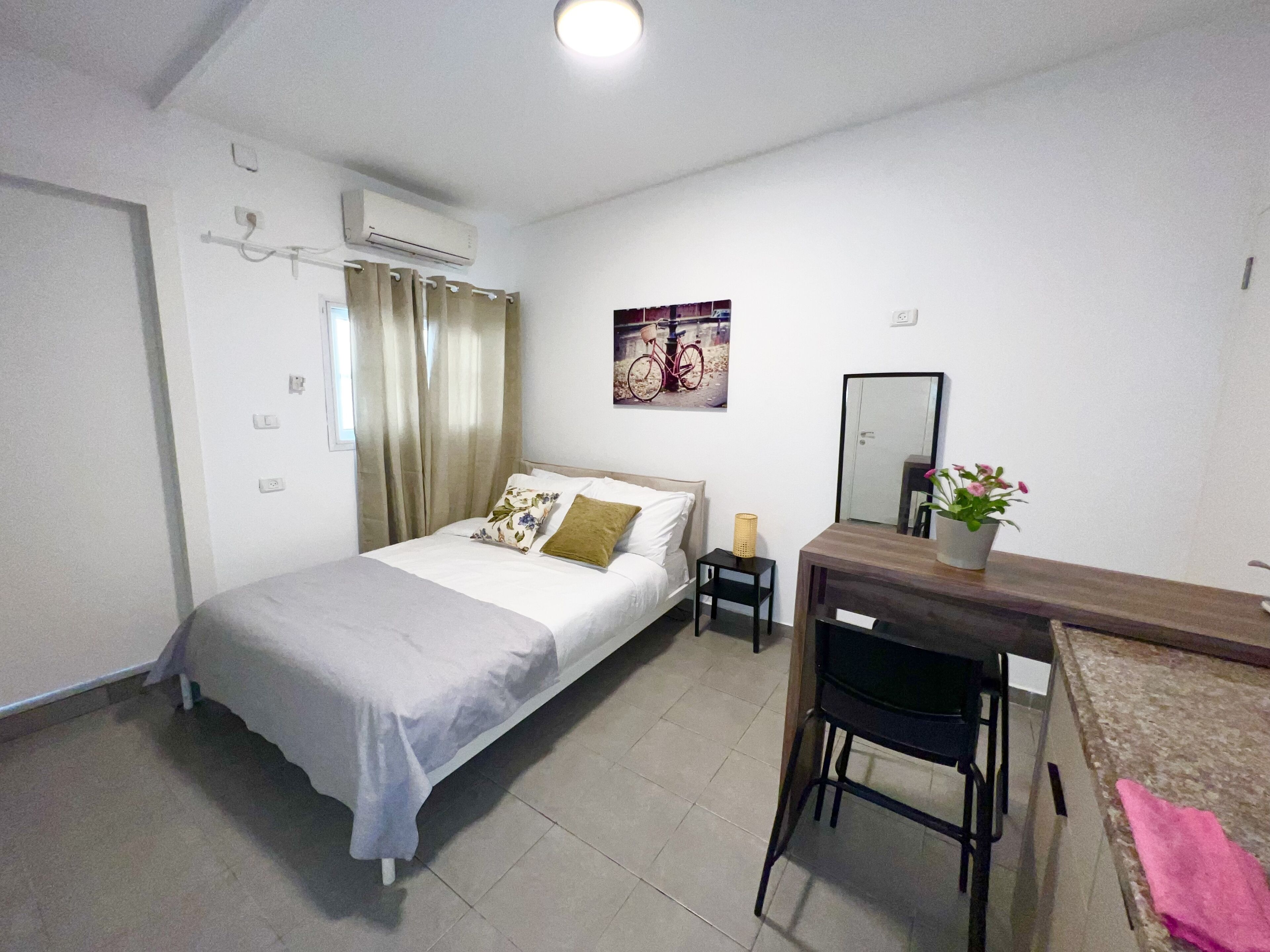 Ein Schlafzimmer mit Bett, Nachttisch, Sessel, Schreibtisch, Spiegel und einer Zimmerpflanze.