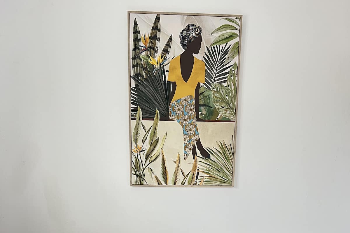 Un dormitorio con una cama, un almohadón verde, un almohadón blanco y una obra de arte enmarcada en la pared.