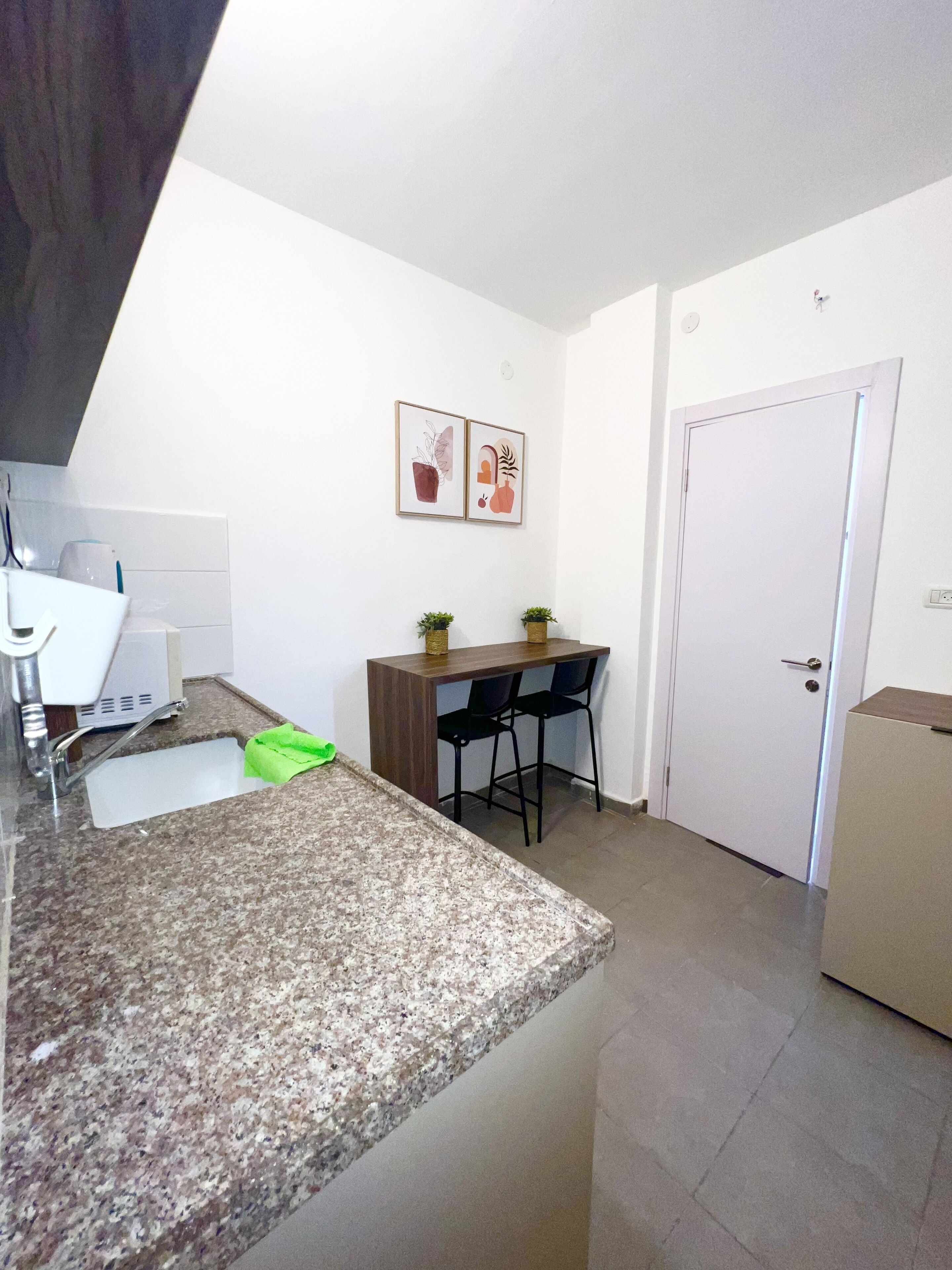 A kitchen with granite countertops, a sink, a wooden table with two chairs, and a white door.