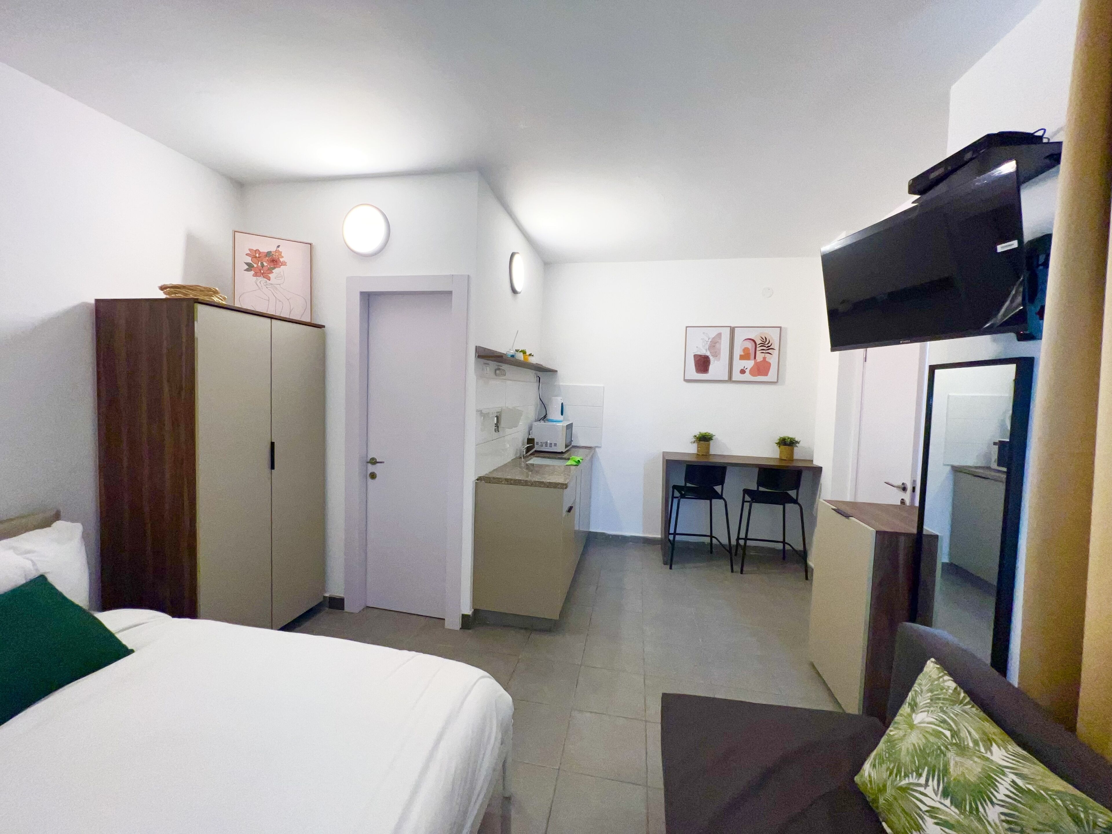 A hotel room with a bed, a wardrobe, a desk with two chairs, a television, and a small kitchenette.