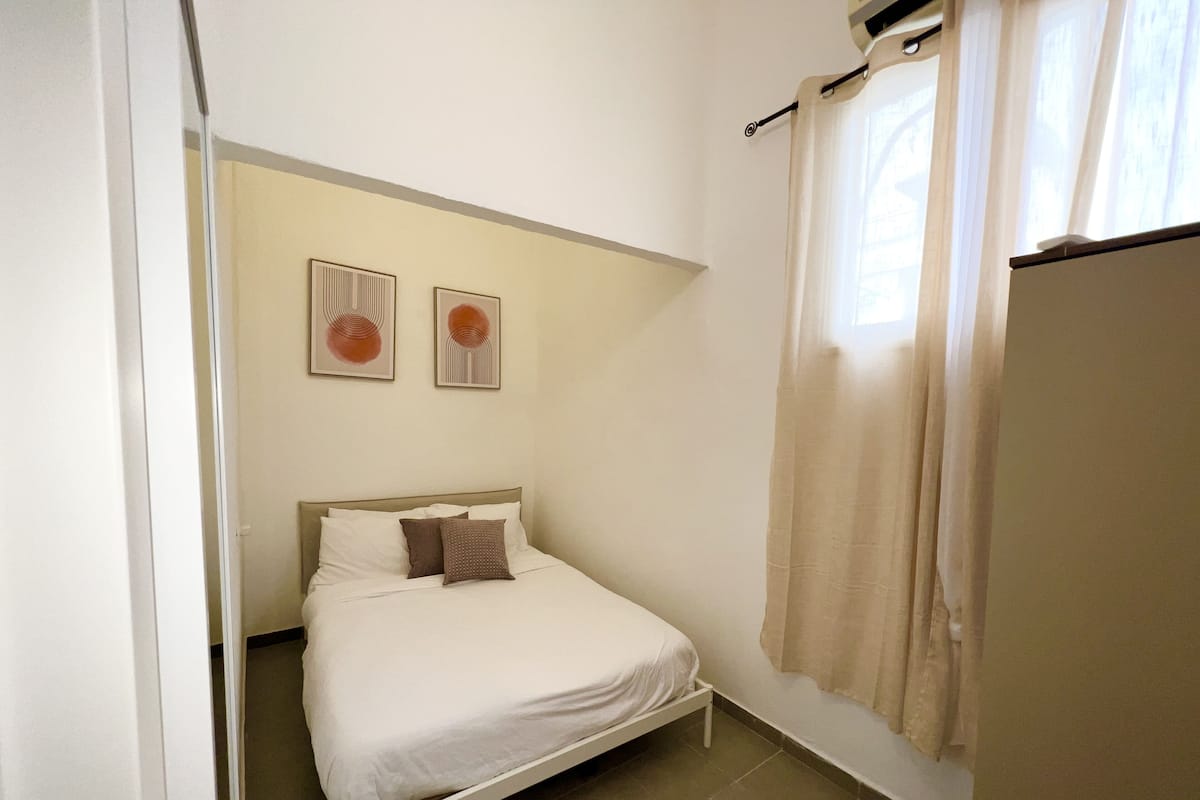 Un dormitorio pequeño y ordenado con una cama individual, una ventana con cortinas y dos obras de arte colgadas en la pared.