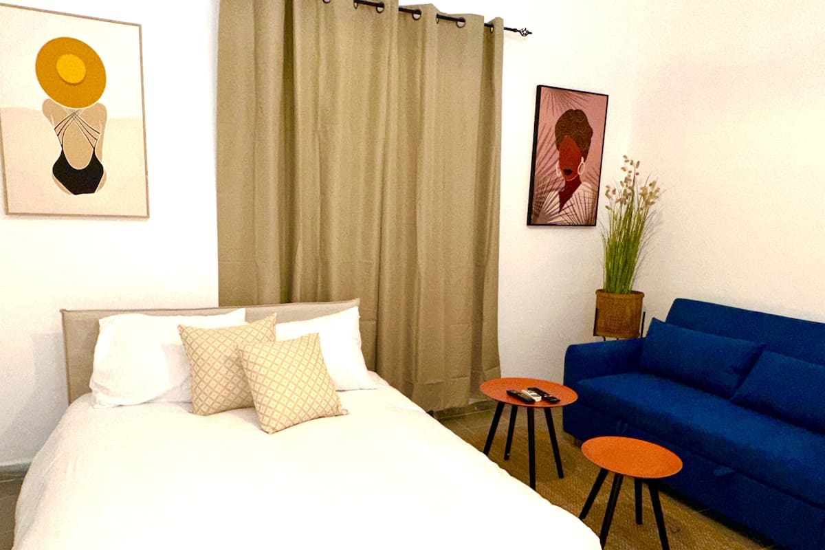 Una habitación de hotel con una cama, un sofá azul, dos mesitas y obras de arte en las paredes.