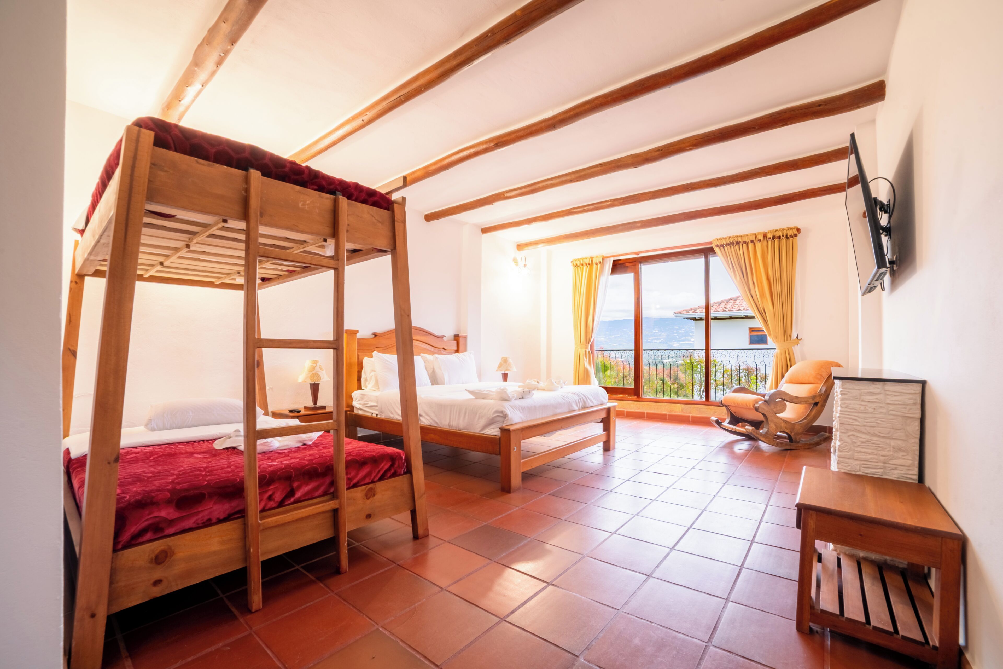 Una habitación con dos literas de madera, una cama individual, un sillón mecedora y un televisor en la pared.