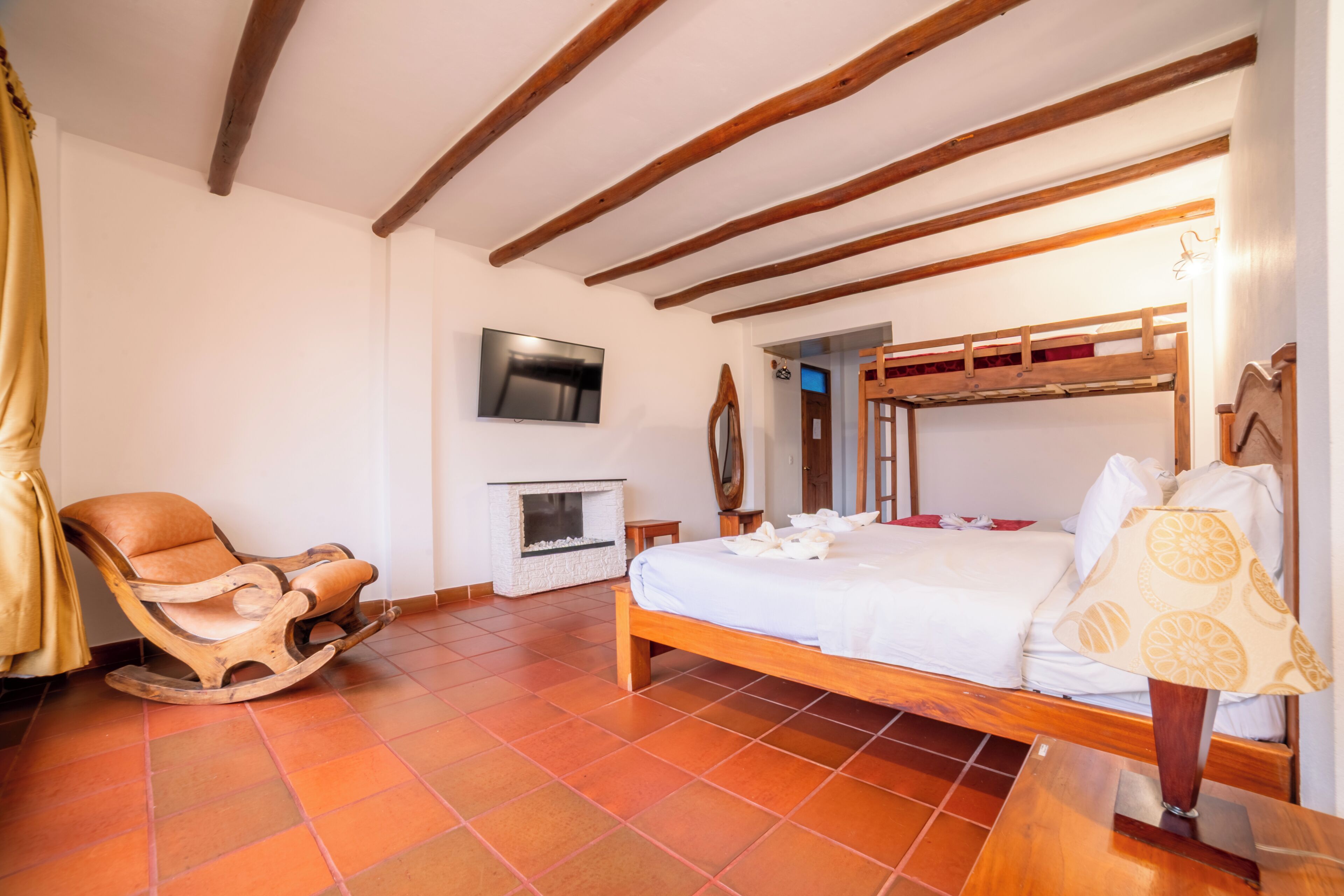 Un dormitorio con una cama de madera, una mecedora, una chimenea y un televisor en la pared.