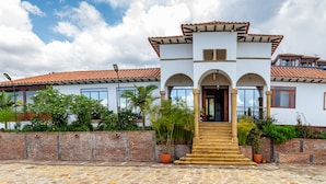 A two-story house with a tiled roof, a central entrance with steps, and a brick wall surrounding the property. - Hotel Cordillera de los Andes  (Villa de Leyva)