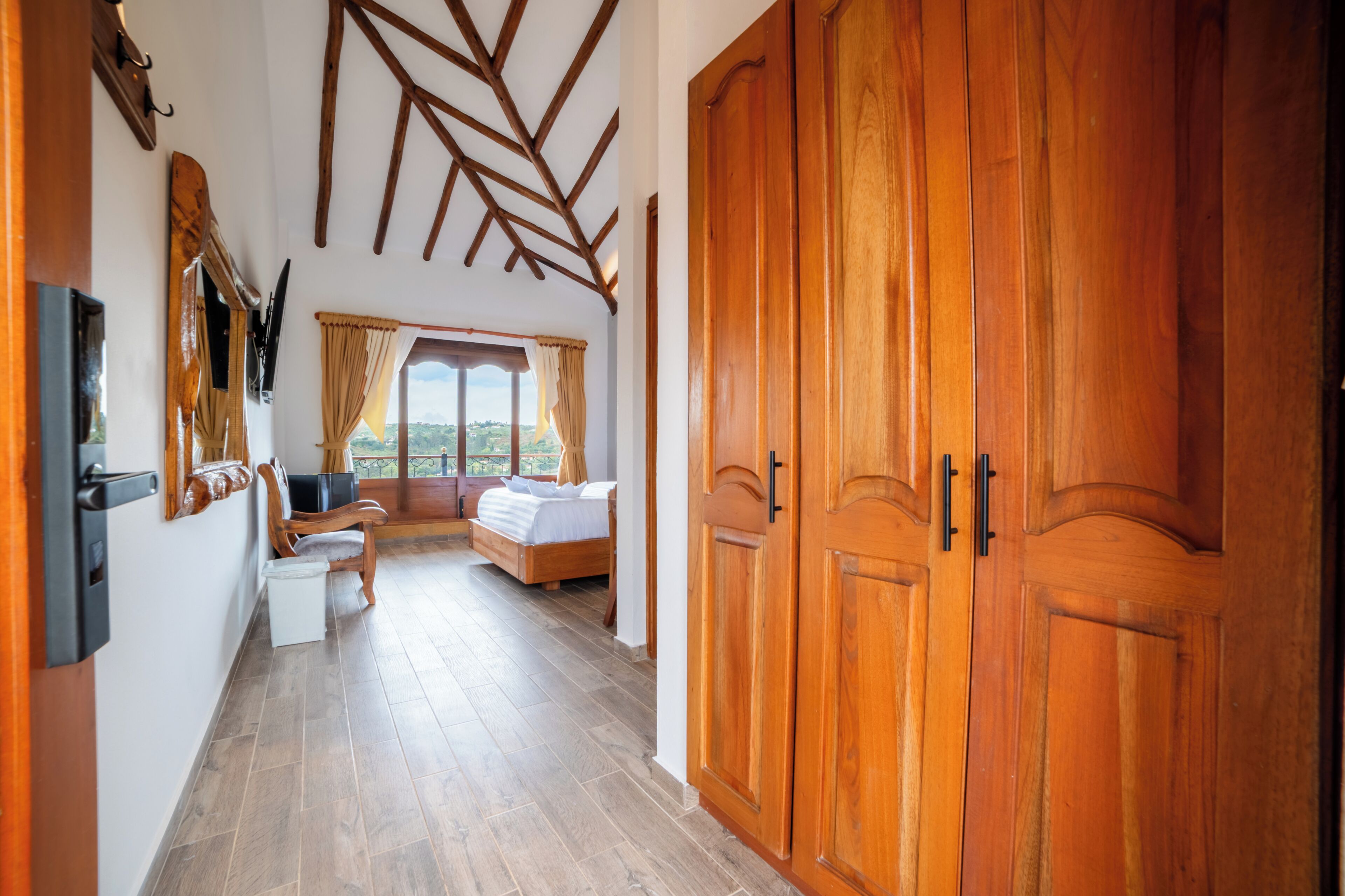 Ein Schlafzimmer mit einem Holzschrank, einem Bett, einem Schreibtisch und einem Fenster mit Vorhängen.