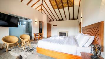 Ein Schlafzimmer mit einem Bett, zwei Korbstühlen, einem Fernseher und einem Kamin.