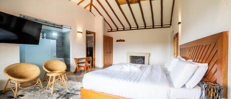A bedroom with a bed, two wicker chairs, a TV, and a fireplace.