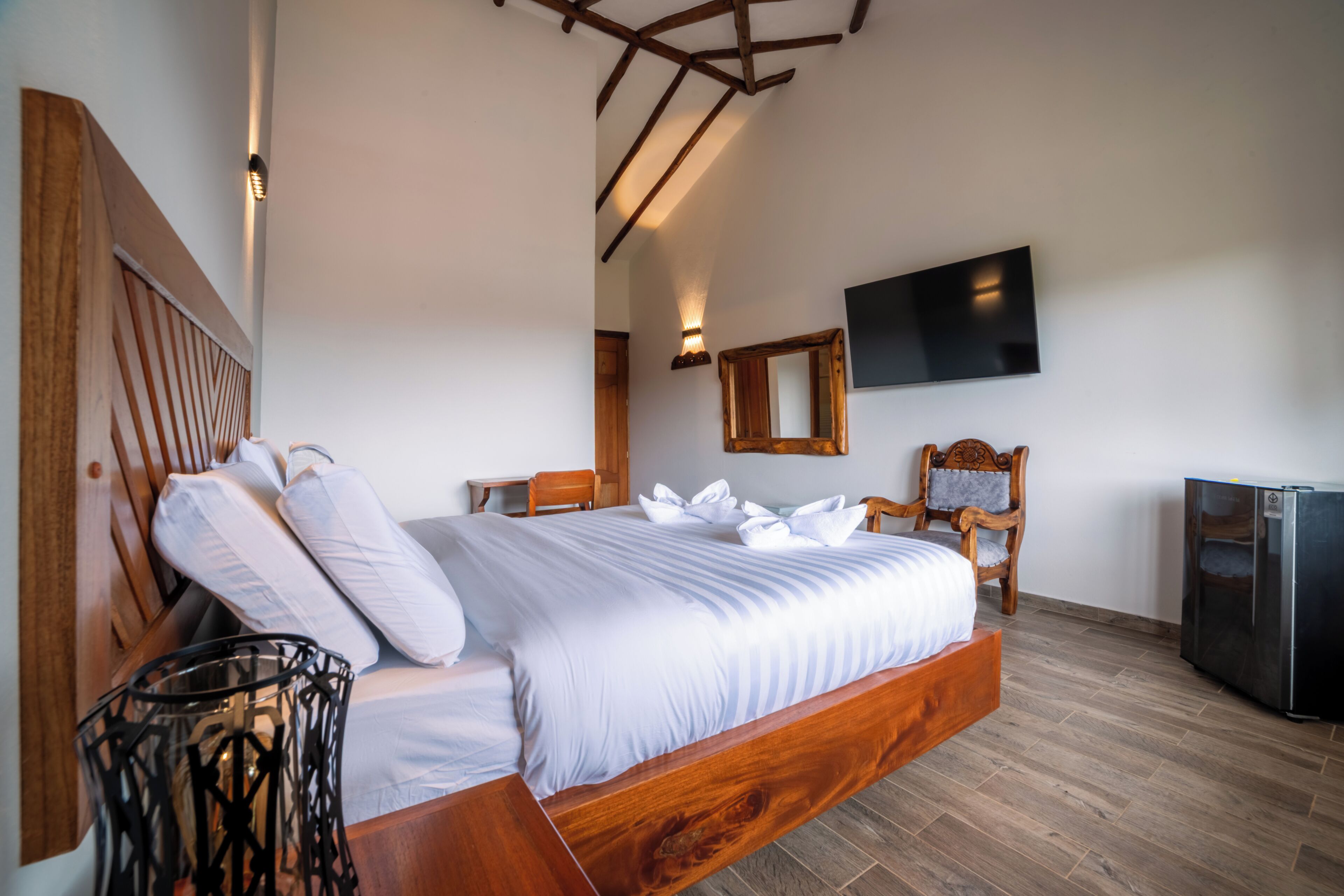 Un dormitorio con cama de madera, televisión de pantalla plana, espejo y refrigerador.