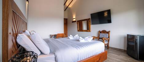 Un dormitorio con cama de madera, televisión de pantalla plana, espejo y refrigerador.