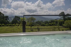A pool with clear water, surrounded by lush greenery and a mountainous landscape in the background.