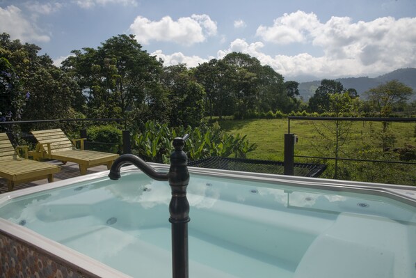 A hot tub with a view of a lush green landscape and mountains in the background.