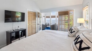 Un dormitorio con una cama grande, televisor, escritorio y vistas al exterior.