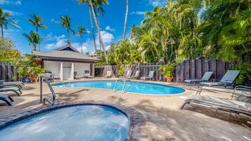 A pool area with lounge chairs and a hot tub, surrounded by palm trees.