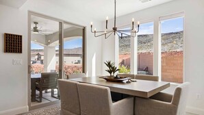 Un comedor con mesa y sillas, una araña y ventanas amplias con vistas a un paisaje desértico.
