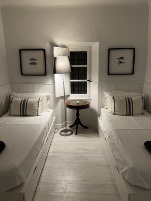A hotel room with two single beds, a round table, a floor lamp, and framed fish pictures on the walls.