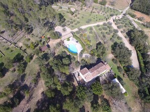 An aerial view of a property with a swimming pool, a large house with a tiled roof, and surrounding greenery.