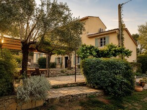A traditional Mediterranean-style house with a stone pathway leading to the entrance, surrounded by lush greenery and a pergola.