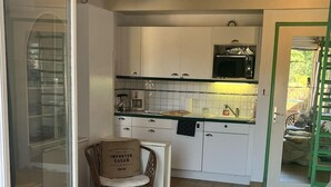 Een ruime woonkamer met een groot raam, een rieten stoel, een bank en een keuken op de achtergrond.