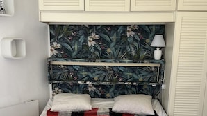 Een bed met een geruit plaid, een bloemrijk hoofdbord en een bedlampje.