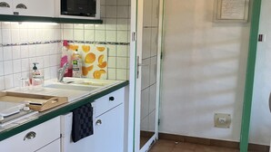 Een keuken met witte kastjes, een magnetron, een spoelbak en een betegelde spatwand.