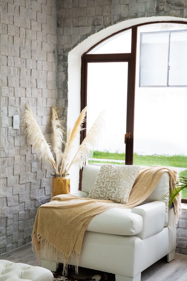 A white sofa with a beige throw blanket, pampas grass in a vase, and a view of a green lawn through a large window. - 15 min from airport! Luxurious Gated Estate with Mountain Views from the Valley. (Tumbaco, Villa Vega)