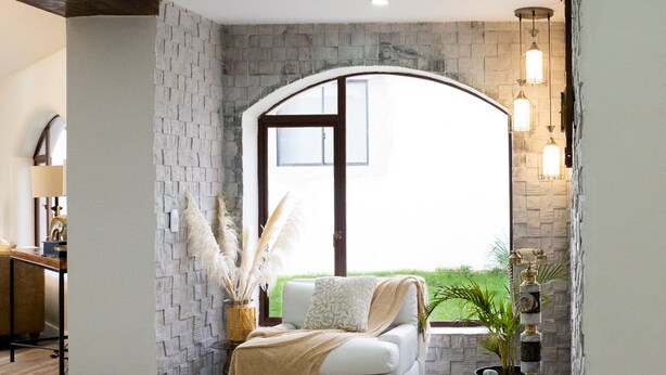 Un salon moderne avec un canapé blanc, un pouf capitonné et un mur d’accent en pierre.