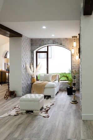 A modern living room with a white sofa, a tufted ottoman, and a stone accent wall. - 15 min from airport! Luxurious Gated Estate with Mountain Views from the Valley. (Tumbaco, Villa Vega)