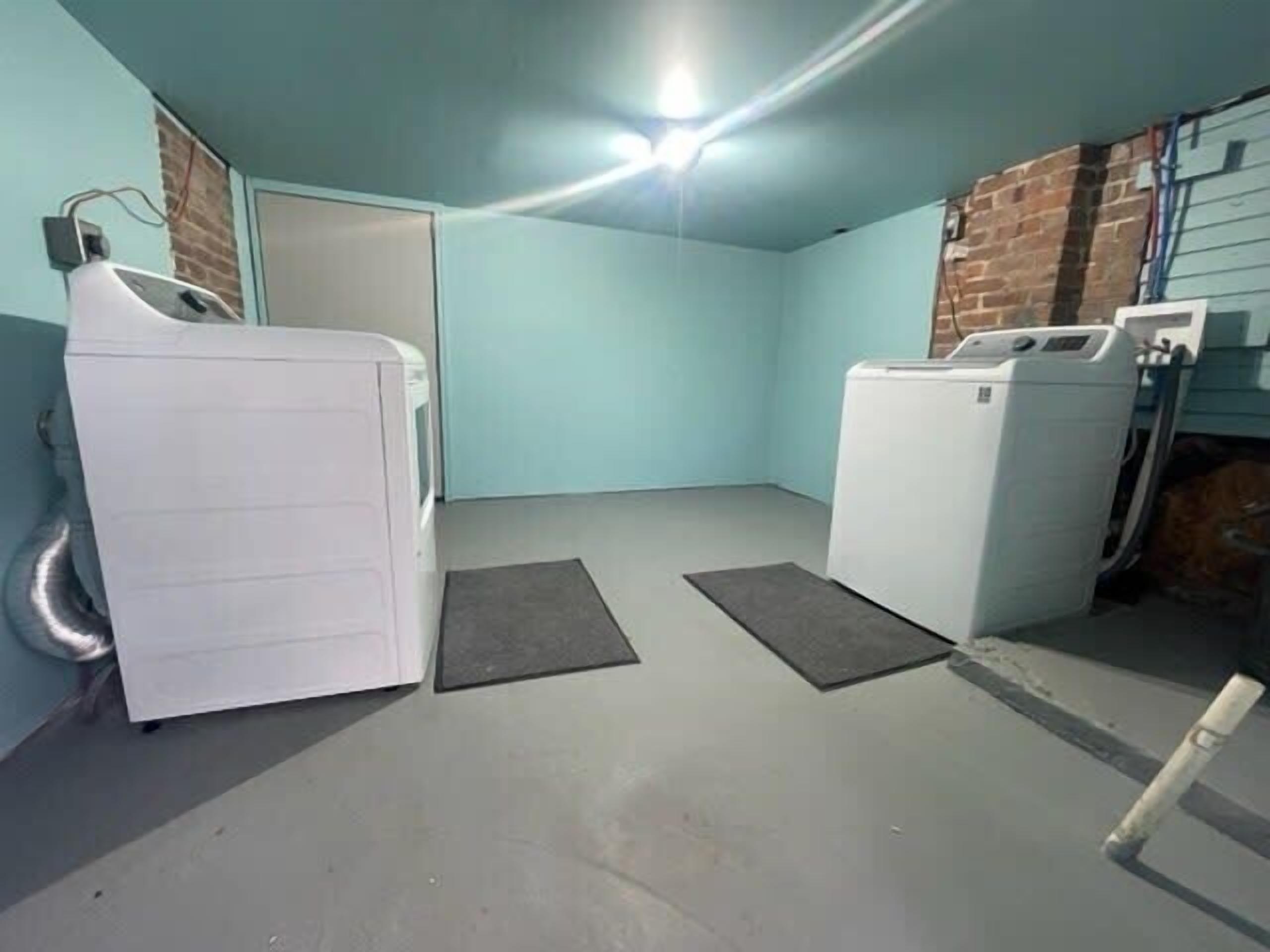 A laundry room with two white washing machines, a grey floor, and a door in the background.