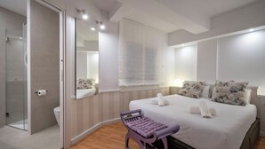 Ein modernes Schlafzimmer mit einem großen Bett, einer Holzbank, einer Duschkabine aus Glas und einem großen Spiegel.