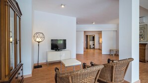 Ein geräumiges Wohnzimmer mit Fernseher, Stehlampe und zwei Korbstühlen.
