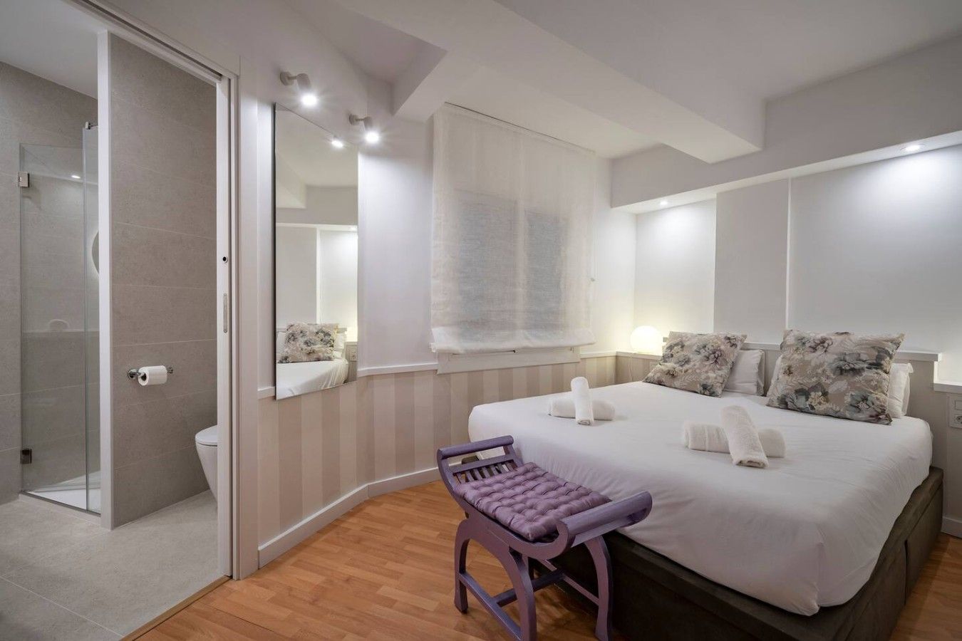 A bedroom with a bed, a bedside table, a chair, a window with curtains, and a mirror.