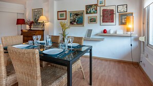 Ein Essbereich mit Korbstühlen, einem Tisch mit Glasplatte und einer weißen Wand mit gerahmten Kunstwerken.