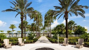 A pathway lined with palm trees leading to a circular seating area with Adirondack chairs and a fire pit. - Escape to Our Beautiful and Comfy Home at Solara (Kissimmee)