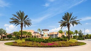 A hotel with a central tower, palm trees, and a landscaped garden with flowers. - Escape to Our Beautiful and Comfy Home at Solara (Kissimmee)